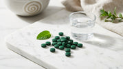 Premium green spirulina tablets arranged on white marble surface with natural lighting, representing ENERGYbits organic spirulina supplements