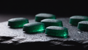 Macro photograph of deep emerald green chlorella algae tablets on dark slate with fine water droplets