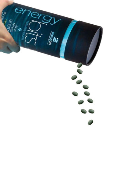 Hand pouring small spirulina tablets from an ENERGYbits® container against a white background.