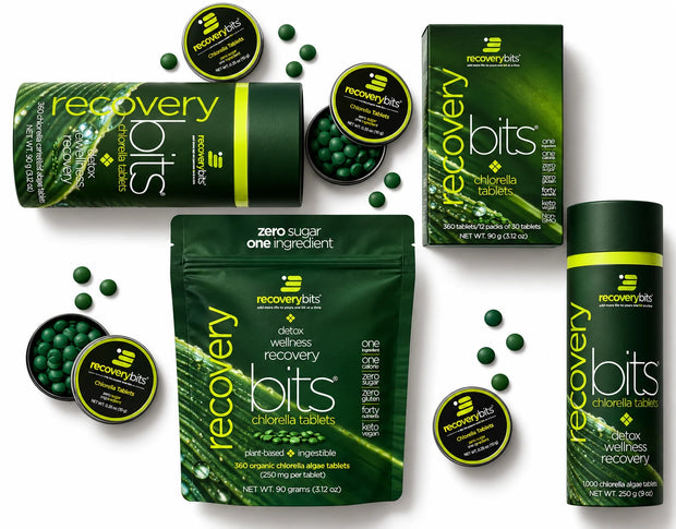 A flat-lay product arrangement of Recovery Bits choline chloride supplement, showing a green and black cylindrical tub, a stand-up pouch, a rectangular box, a canister, and several open round jars filled with dark green round tablets on a white background.