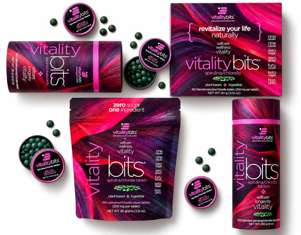 Vitality Bits dietary supplement packaging arranged on a white background, including a stand-up pouch, cylindrical bottle, box, and round jars, with loose dark green tablets scattered around. The packaging features a vivid magenta, purple, and black abstract design with white and pink typography.