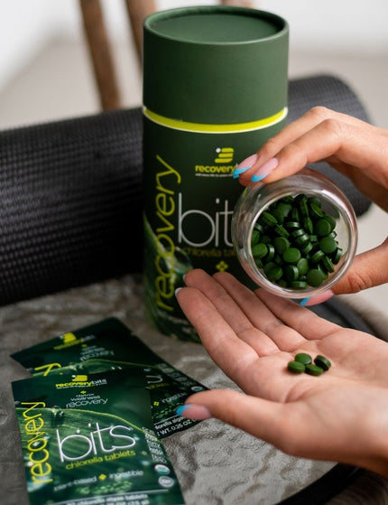 Woman's hand pouring ENERGYbits® chlorella tablets from a jar into her palm. ENERGYbits® chlorella supplement packaging in the background.